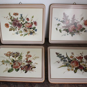 K&ouml;nnte beinhalten: Vier quadratische Tischsets mit Blumendesigns. Jedes Tischset hat einen cremefarbenen Hintergrund mit einer anderen Anordnung von Rosen, Tulpen und anderen Blumen in Rosa, Rot und Lila. Ein hellbrauner Rand umrahmt jedes Tischset.