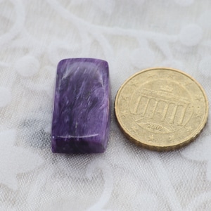 Könnte beinhalten: Ein rechteckiger Cabochon-Edelstein in Lila und Grau neben einer 1-Euro-Münze aus dem Jahr 2002.