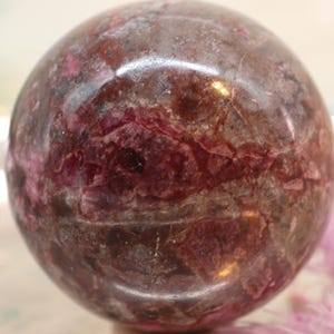 Könnte beinhalten: Eine polierte Kugel aus rosa und grauem Rhodochrosit, einem natürlichen Edelstein. Die Kugel hat eine glatte, polierte Oberfläche und ein wirbelndes Muster aus Rosa und Grau.