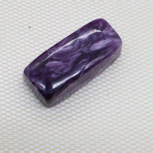 Può includere: Una pietra preziosa cabochon di colore viola e bianco con un motivo a spirale. La pietra preziosa è lucidata e ha una superficie liscia.