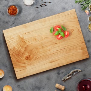 May include: A rectangular wooden cutting board with a light brown finish. Garnished with sliced tomatoes and basil. Accompanied by spices, a corkscrew, and a glass of red wine. Ideal for food preparation and serving.