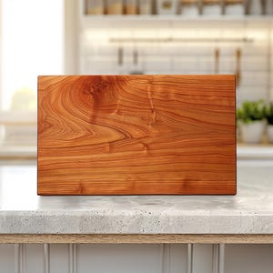 May include: A rectangular wooden cutting board with a rich, reddish-brown color and visible wood grain. The board is displayed on a light-colored countertop, suggesting a kitchen setting. The wood appears to be finely finished.
