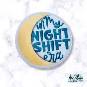 May include: A white round sticker with a yellow crescent moon and blue text that reads "in my night shift era".