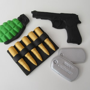 May include: A collection of toy military items: a black handgun, a green grenade, a black bandolier with yellow bullets, and two silver dog tags. One tag reads "HAPPY BIRTHDAY".