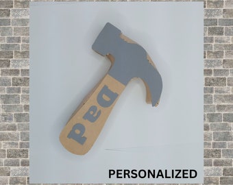 Könnte beinhalten: Ein grauer und brauner Kartonhammer mit dem Wort "Papa" auf dem Griff. Der Hammer ist ein personalisiertes Handwerk.