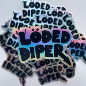 May include: A stack of iridescent stickers with the text "Loaded Diper" in black lettering. The stickers have a holographic finish and a rainbow gradient.