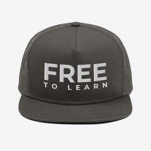 May include: A dark gray trucker hat with a white mesh back. The front of the hat has the words "FREE TO LEARN" embroidered in white.