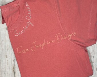 May include: A coral pink t-shirt with the text "Sewing Queen" embroidered on the front. The text "Teresa Josephine Designs" is also embroidered on the shirt.