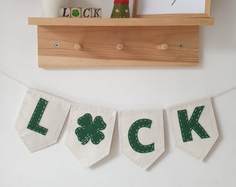 May include: A white felt banner with green felt letters spelling "LUCK" and a green felt shamrock between the "C" and "K".