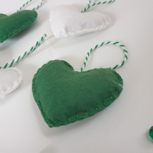 May include: A garland of green and white felt hearts with white twine string. The hearts are sewn with white thread and have a slightly textured surface.