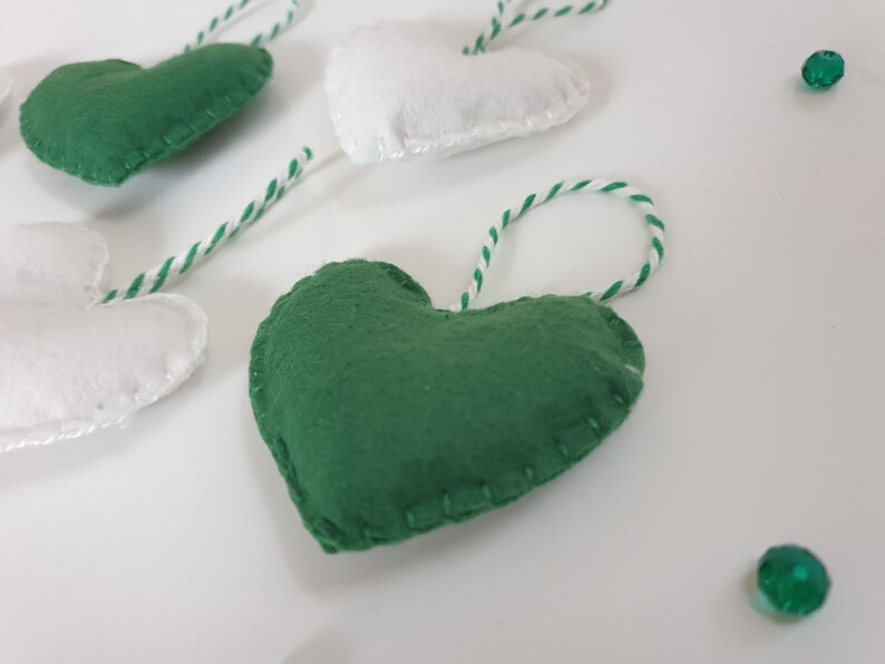 May include: A garland of green and white felt hearts with white twine string. The hearts are sewn with white thread and have a slightly textured surface.