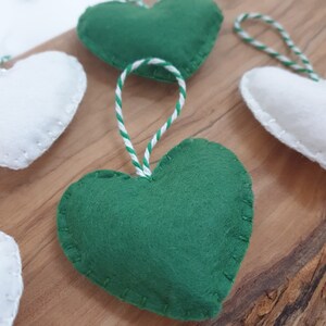 May include: A set of felt heart ornaments with white and green stitching. The hearts are strung together with white and green twine.