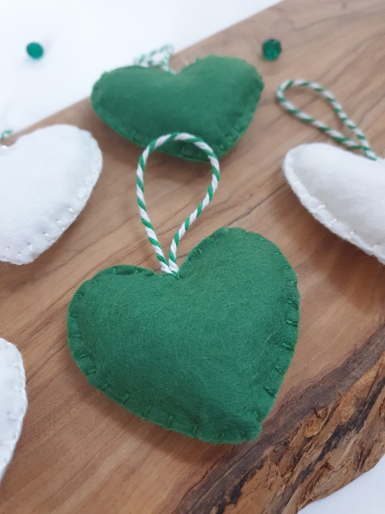 May include: A set of felt heart ornaments with white and green stitching. The hearts are strung together with white and green twine.