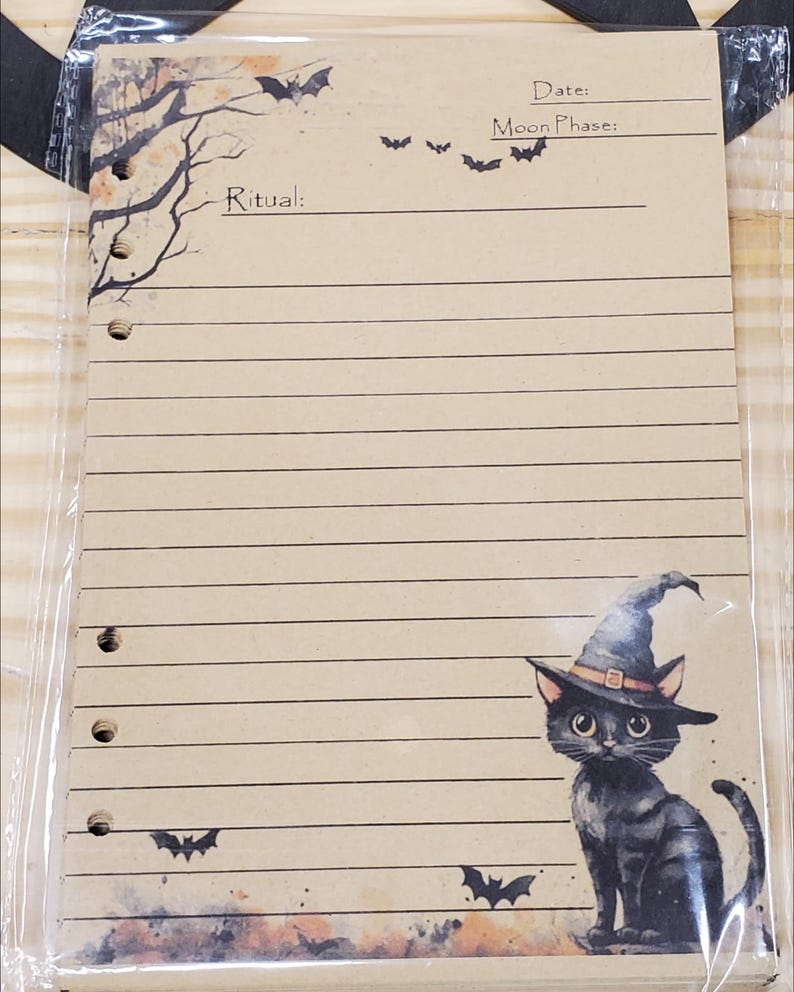 Op de afbeelding: Een bruine papieren journalpagina met een zwarte kat die een heksenhoed draagt. De pagina heeft lijnen om op te schrijven en bevat de tekst "Ritueel:", "Datum:" en "Maanfase:". Er zijn ook zwarte vleermuizen getekend op de pagina.