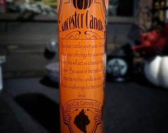 Può includere: Candela di vetro arancione con la scritta "Ancestor Candle" e un'illustrazione di zucca. La candela ha il testo che recita "Metti la tua candela sul tuo Altare o vicino alle tue offerte per i tuoi cari..." e "BlackCat Curiosity Co."