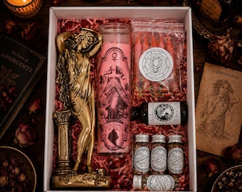 Pode incluir: Uma caixa de presente ritual contendo uma estátua de Afrodite em tom dourado, uma vela pilar rosa alta com imagem de Afrodite, um saco de velas vermelhas pequenas, um frasco de óleo ritual e quatro potes de vidro com ervas secas.