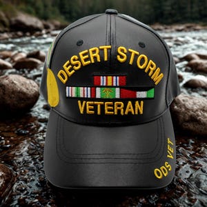 Puede incluir: Gorra de béisbol negra con la inscripción dorada "Desert Storm Veteran". La gorra presenta cintas de colores y el texto "ODS VET" en el lateral. La gorra está hecha de un material similar al cuero.