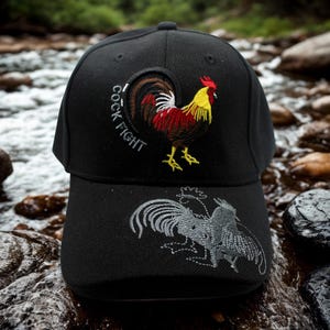 May include: Black baseball cap with a rooster design. The cap has the text "COCK FIGHT" and a detailed image of a rooster in red, yellow, and brown. The brim features a gray embroidered rooster.
