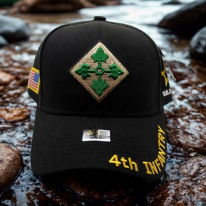 May include: Black baseball cap featuring a gold and green emblem with a cross design. The cap has the text "4th INFANTRY" in yellow embroidery on the side and a small American flag patch. A stylish accessory for outdoor activities.