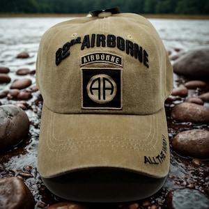 Puede incluir: Gorra de béisbol color caqui con texto bordado en negro "82nd AIRBORNE". La gorra presenta un parche con "AIRBORNE" y "AP" en negro y dorado. La visera es negra y "ALL THE WAY!" está bordado en el lateral.