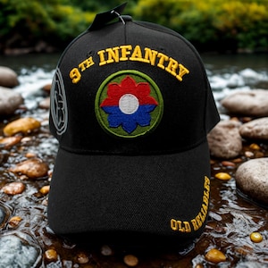May include: Black baseball cap with embroidered text and a colorful patch. The cap features "9th Infantry" in yellow, a circular patch with red, blue, and white details, and "OLD RELIABLES" in yellow. The cap is set against a natural background.