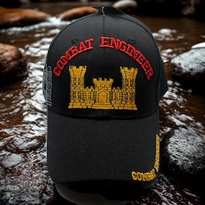 May include: Black baseball cap with "COMBAT ENGINEER" embroidered in red and gold. The cap features a gold castle emblem and additional text on the side and brim. A stylish accessory.