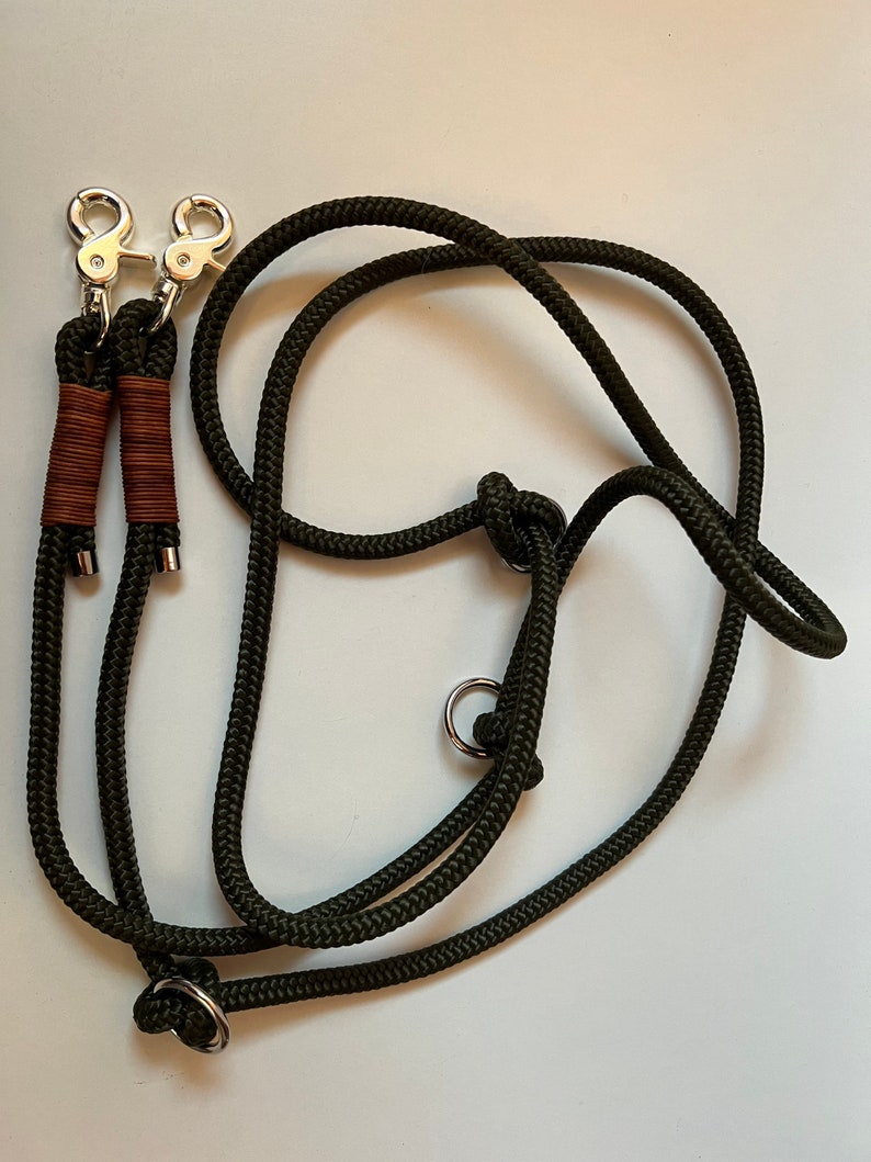 May include: A green double dog leash with two silver clips and two silver rings. The leash is made of thick rope.