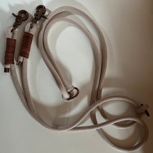 May include: A beige rope dog leash with two brass clasps and a brown leather accent.