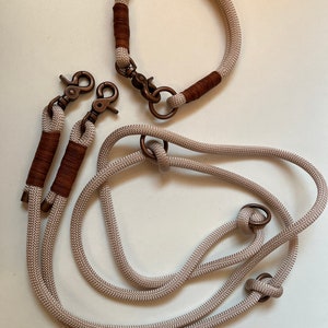 May include: A set of two dog leashes and a matching collar made of beige rope with brown leather accents. The leashes have two metal clips and the collar has a metal buckle.