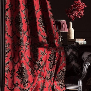 May include: Red and black damask curtains with a floral design. The curtains are draped, showing a dark interior with a lamp, vase, and chair. The fabric has a luxurious sheen.