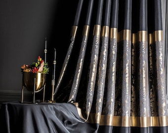 Puede incluir: Cortinas negras con ribete dorado y un patrón geométrico. Las cortinas cuelgan frente a una pared oscura. Un soporte de metal dorado con una parte superior redonda y tres patas sostiene un jarrón con flores rojas y naranjas.