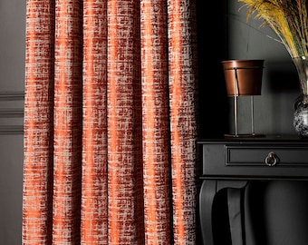 May include: Orange and white patterned curtains with a textured woven fabric. The curtains are hanging in a room with a black side table and a vase with dried flowers.
