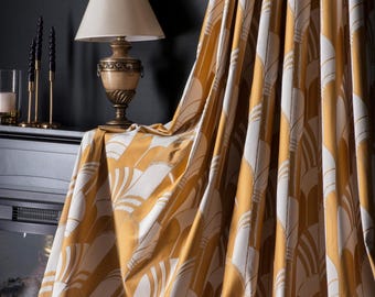 May include: Mustard yellow and white patterned curtains. The fabric drapes over a table with a lamp and decorative items. The curtains have a repeating fan-like design, creating a vintage aesthetic. The room has a dark gray wall.
