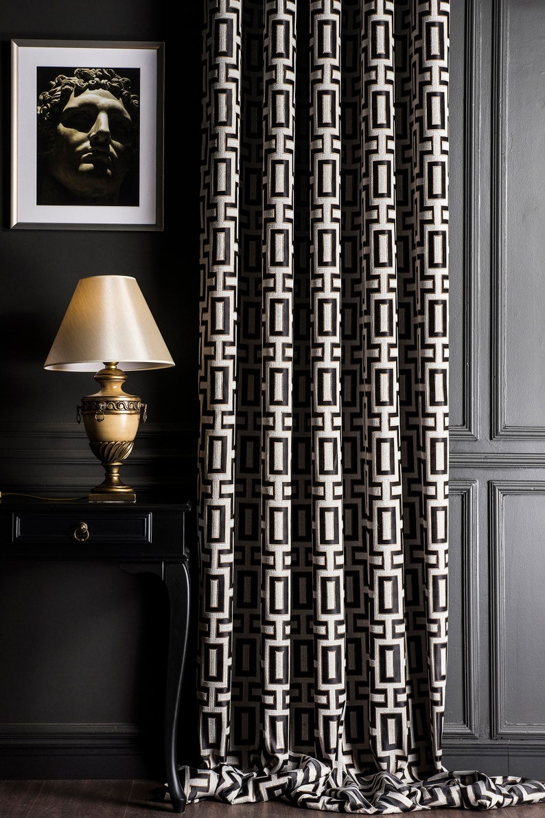 May include: Black and white geometric patterned curtains with a black lamp and a framed picture of a sculpture on a black side table.