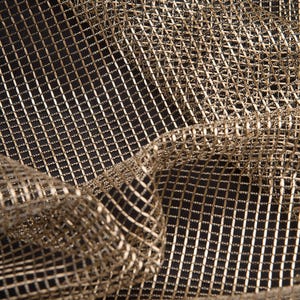 Peut inclure: Gros plan sur un tissu en maille métallique dorée avec un motif en grille de diamants. Le tissu est drapé, créant des plis et des ombres douces sur un fond noir. La texture est complexe et détaillée.
