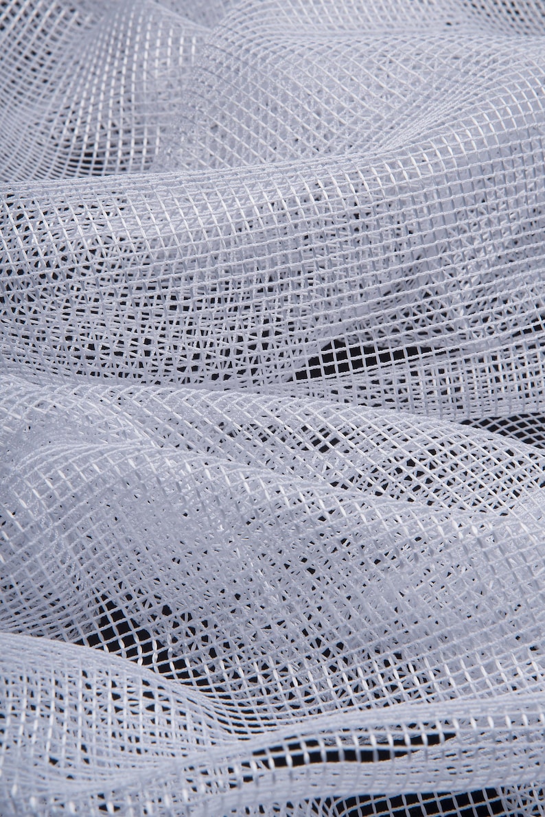 Pode incluir: Close-up de tecido de malha branco com um padr&atilde;o de grade. O tecido &eacute; drapeado e dobrado, criando sombras e texturas. O material parece macio e leve, com uma qualidade ligeiramente transl&uacute;cida. O fundo &eacute; escuro, enfatizando o branco brilhante do tecido.