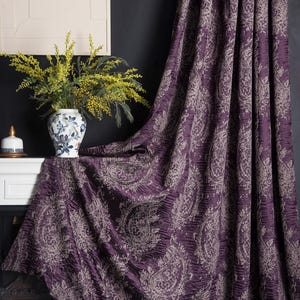 May include: A rich purple curtain with a paisley design, shown draped. The fabric has a textured appearance. A vase of yellow flowers and a candle sit on a white mantelpiece. Home furnishings.
