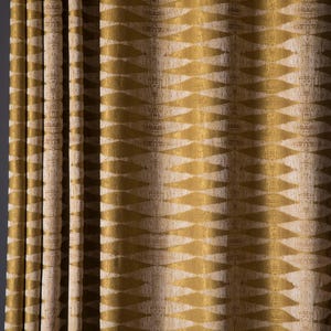 May include: Close-up of a beige and gold curtain with a repeating geometric pattern. The design features a series of diamond shapes in a golden hue against a neutral background. The fabric is draped in vertical folds.