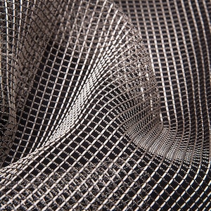 May include: Close-up of a metallic silver and black mesh fabric. The fabric is draped, creating folds and shadows that highlight the intricate grid pattern. The material has a shiny, reflective quality.
