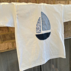 May include: White t-shirt with a blue and white sailboat design sewn on the back.