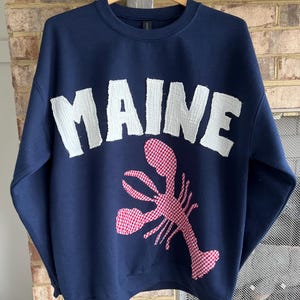 May include: A navy blue sweatshirt with a white "MAINE" applique and a red and white gingham lobster applique.