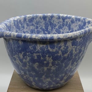 May include: A mixing bowl featuring a blue and white speckled pattern throughout the exterior and interior. The bowl has a wide, rounded rim with two prominent, curved pouring spouts extending from opposite sides of the circular opening.