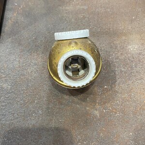 May include: A vintage brass light socket with a white ceramic interior and a white threaded cap. The socket has a tarnished, aged appearance, suggesting it is an antique or a reproduction of an older design. The interior shows the electrical contacts.