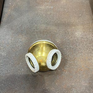 May include: A brass-colored light fixture with two white, ring-shaped components. The fixture has a rounded shape and a threaded base. The text "Benjamin" and "1993" is visible on the fixture.