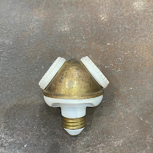May include: A vintage brass and white light fixture with three sockets. The fixture has a conical brass body with three white, circular sockets. The base is white with a brass screw-in bulb socket.