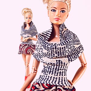May include: Two dolls with blonde hair styled in high buns, wearing black and white textured cowl-neck tops paired with skirts featuring a red, black, and white swirling pattern. The dolls have articulated joints at the shoulders and elbows.