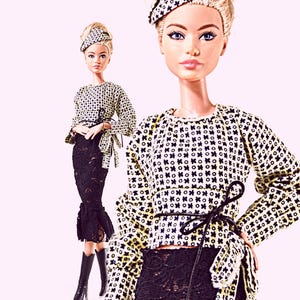 May include: A fashion doll wearing a long-sleeved top with a black and white geometric pattern, a black lace skirt, and a matching patterned beret. The doll has blonde hair styled in an updo and is wearing black knee-high boots.