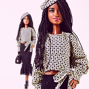 Könnte beinhalten: Eine Modepuppe trägt ein cremefarbenes Oberteil mit einem schwarzen geometrischen Muster, ein passendes Barett und einen schwarzen Spitzenrock. Die Puppe trägt außerdem eine schwarze Handtasche und schwarze Plateau-Stiefel. Die Puppe hat lange schwarze Haare.