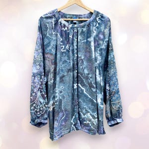 May include: A long-sleeved, blue and white patterned shirt with a button-up front. The shirt has a gathered neckline and a relaxed fit.