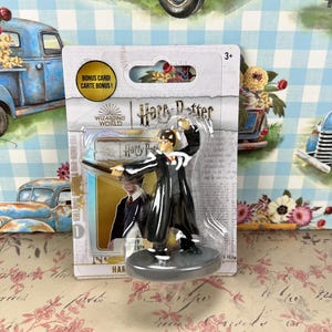 May include: A Harry Potter figurine in a clear plastic package. The figurine is of Harry Potter in a black robe, holding a wand. The package includes the text "Harry Potter" and "Bonus Card!"
